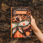 Book titled 'Wild Child: Nature Craft Projects for Kids' held by a hand against a textured brown background