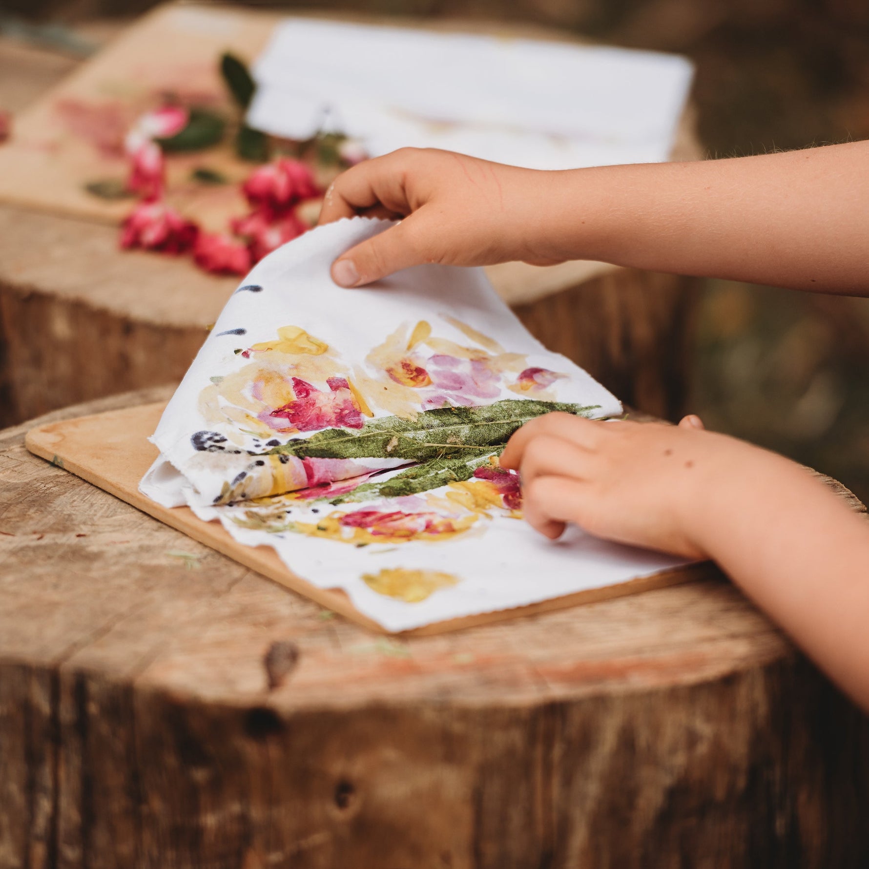 Hands arranging flowers on a piece of fabric on a wooden surface outdoors