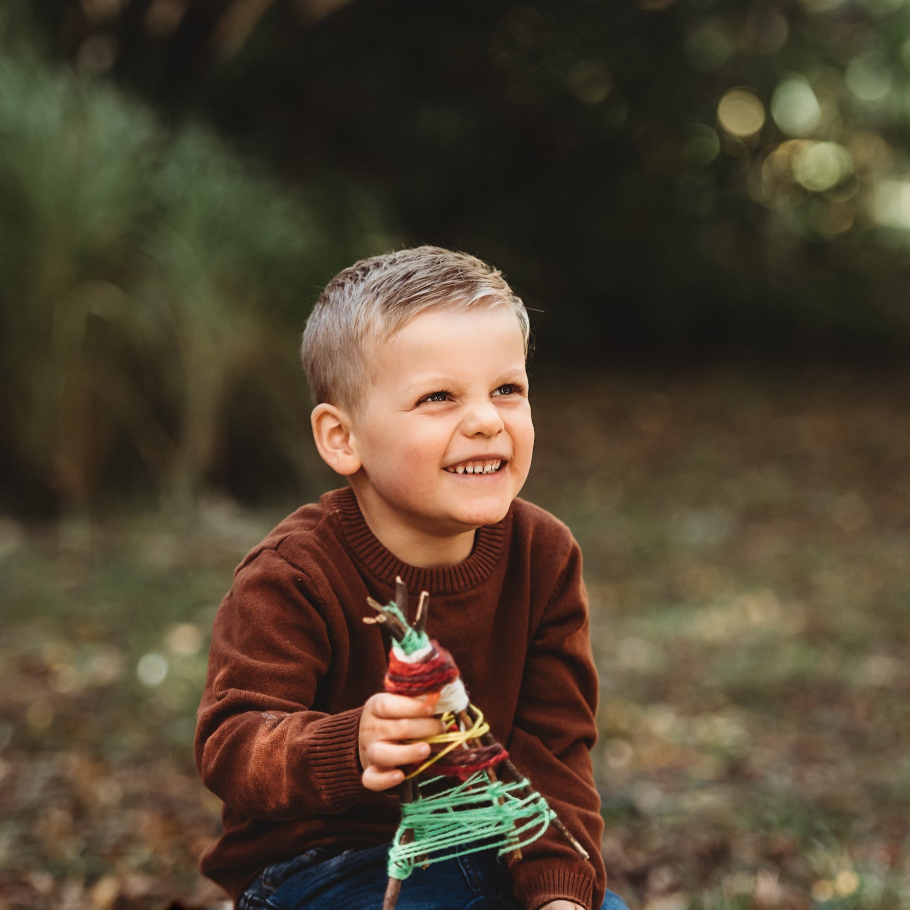 Child holding a small Christmas tree in a forest setting.