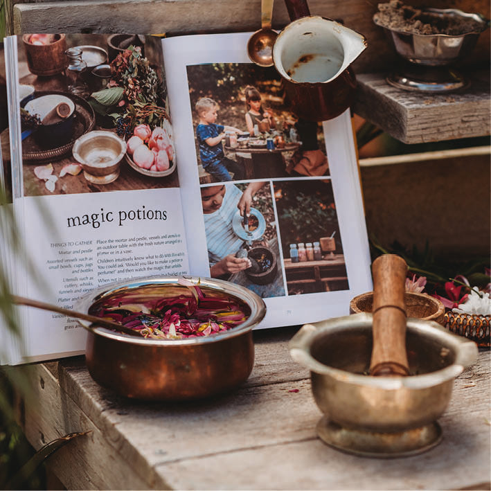 Copper pots with colorful contents on a wooden surface next to an open book titled 'magic potions'.