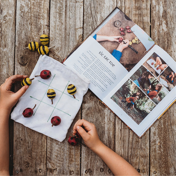 Children playing with a tic-tac-toe game made of natural materials on a wooden surface.