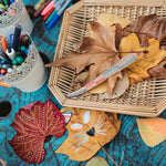 Colorful markers in a container with painted leaves on a textured surface