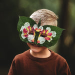 Child wearing a floral mask made of leaves and flowers against a dark background