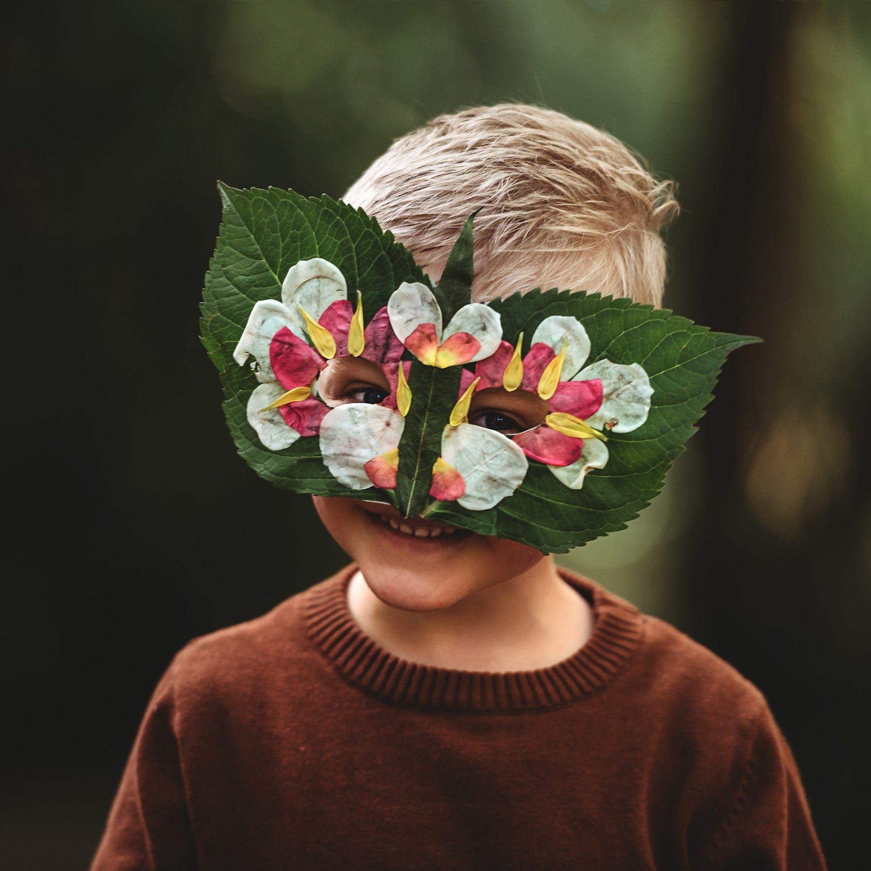 Child wearing a floral mask made of leaves and flowers against a dark background