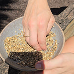 Person holding a small dish with soil and seeds, outdoors.