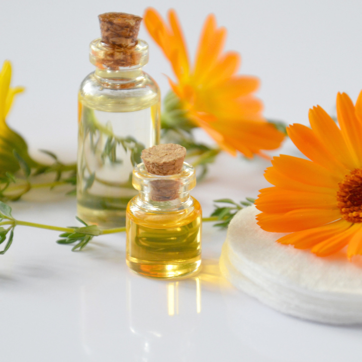 Two small glass bottles with cork lids on a white surface with orange flowers.