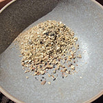 Small pile of seeds with vermiculite in a ceramic bowl on soil.